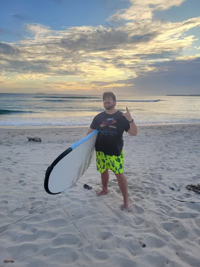 Andy with a surfboard at sunset on the beach